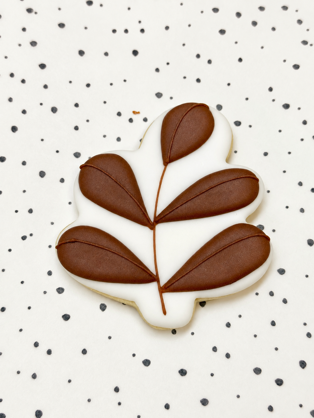Koekje met bruine herfstbladeren op witte royal icing, op een gestippelde ondergrond.