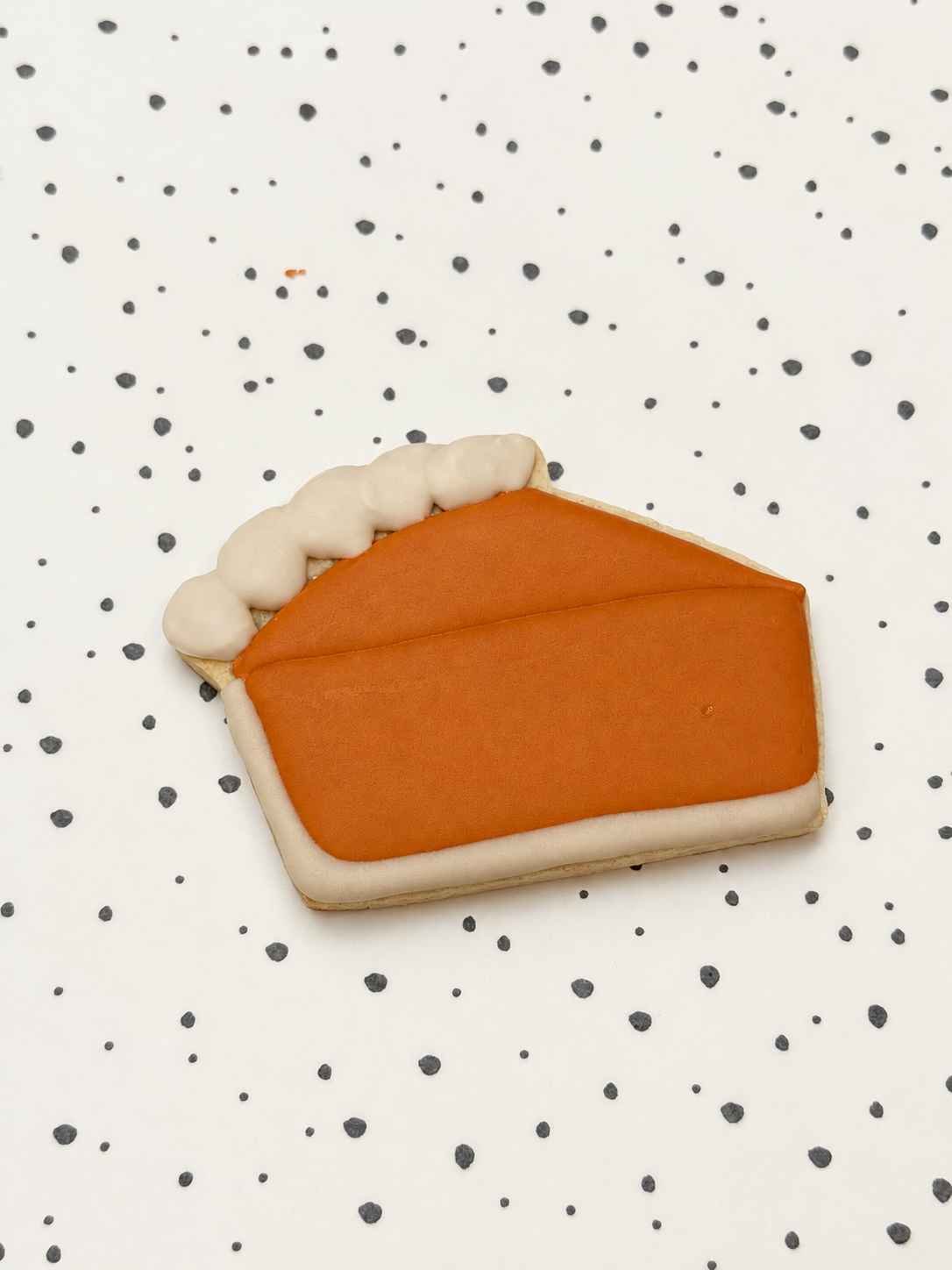 Koekje in de vorm van een taartpunt met oranje royal icing en een witte korstrand, op een gestippelde ondergrond.