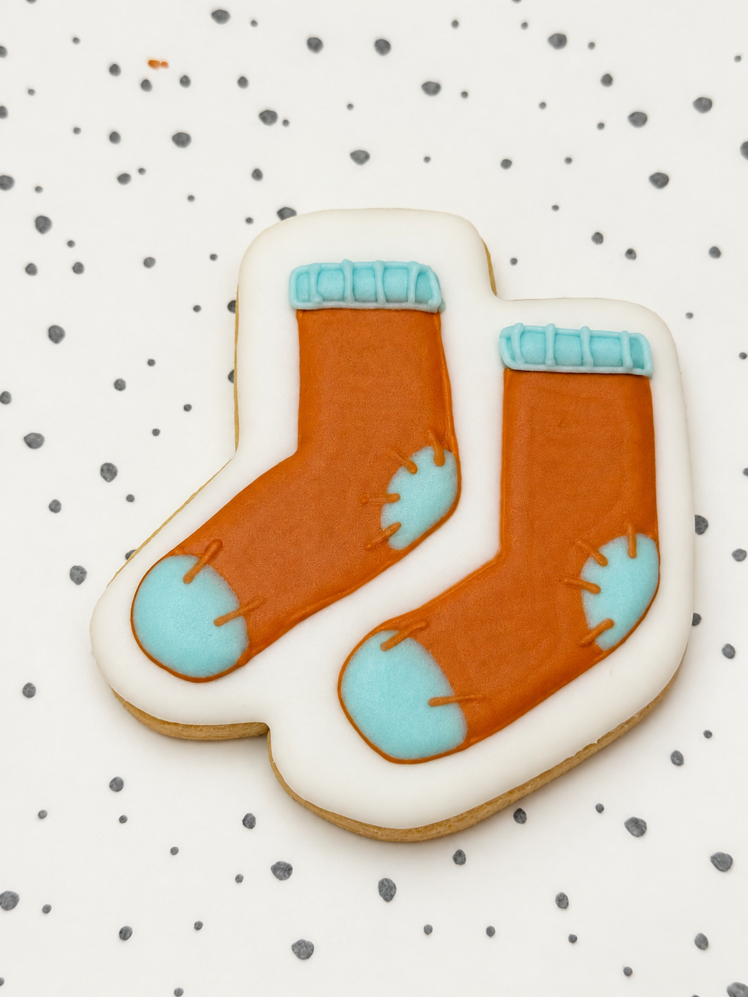 Koekje in de vorm van twee oranje sokken met lichtblauwe boorden, hielen en tenen, op een gestippelde ondergrond.